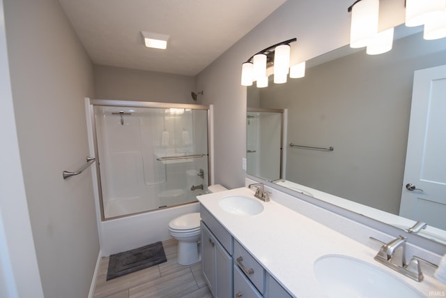 bathroom featuring a sink, bath / shower combo with glass door, toilet, and double vanity
