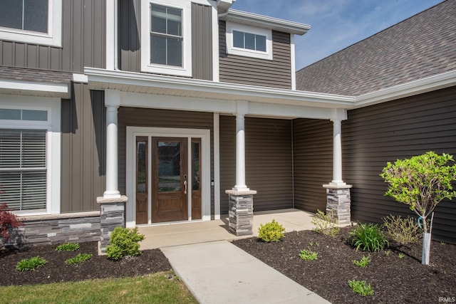 view of exterior entry featuring a shingled roof, covered porch, and board and batten siding
