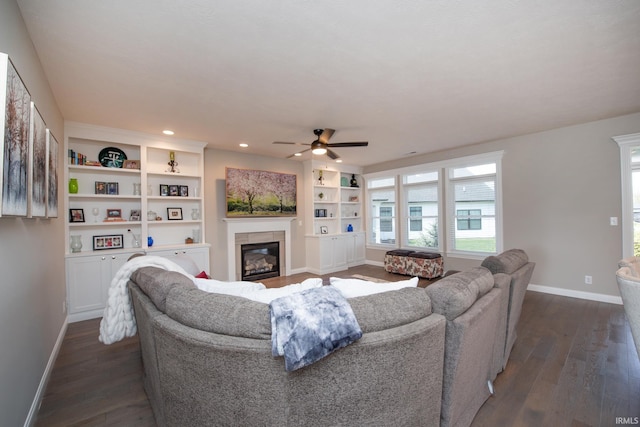 living area featuring a ceiling fan, baseboards, dark wood finished floors, and a glass covered fireplace