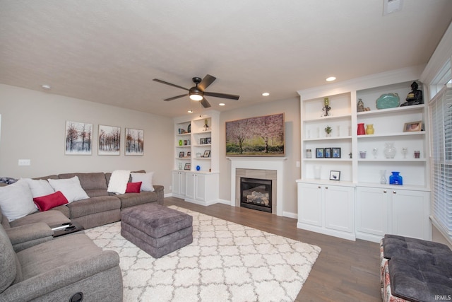 living room with dark wood-style floors, recessed lighting, built in shelves, a tile fireplace, and a ceiling fan