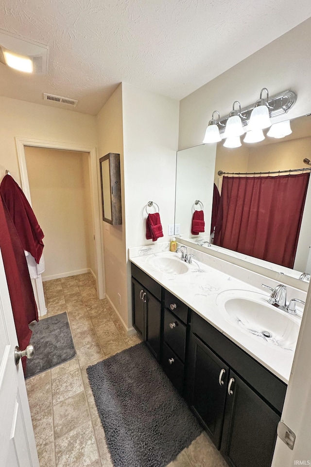 bathroom with double vanity, a textured ceiling, visible vents, and a sink
