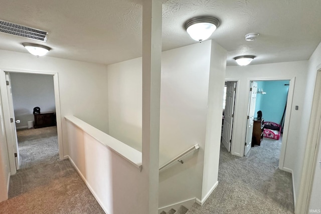 corridor with visible vents, baseboards, carpet floors, and an upstairs landing