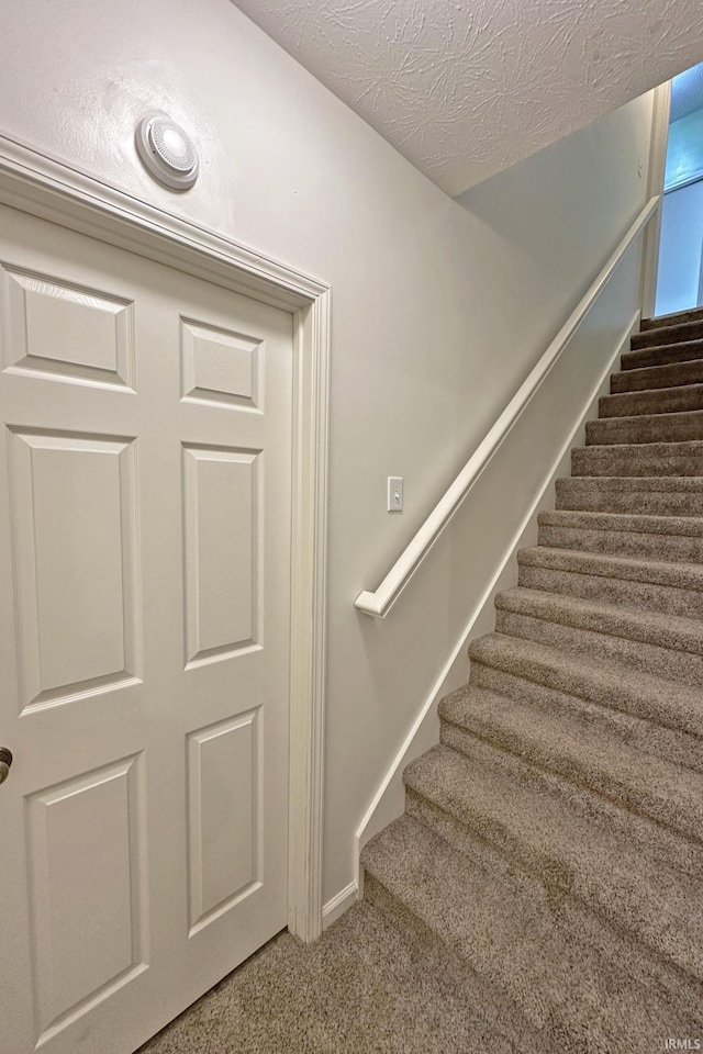 stairway with a textured ceiling, baseboards, and carpet