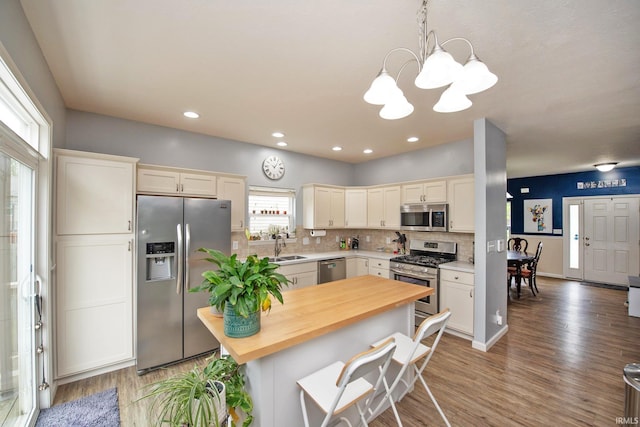 kitchen featuring an inviting chandelier, butcher block counters, light wood-type flooring, appliances with stainless steel finishes, and backsplash