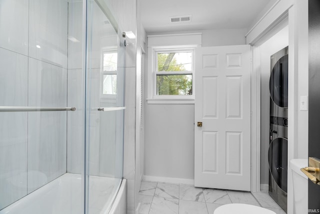 full bathroom featuring shower / bath combination with glass door, toilet, stacked washing maching and dryer, marble finish floor, and visible vents