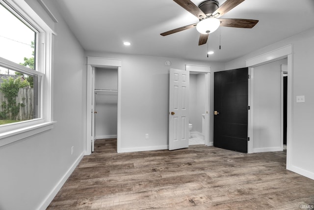 unfurnished bedroom featuring a walk in closet, ensuite bath, recessed lighting, baseboards, and wood finished floors