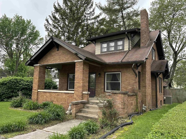 view of front of house with a chimney, brick siding, central AC, fence, and a front lawn