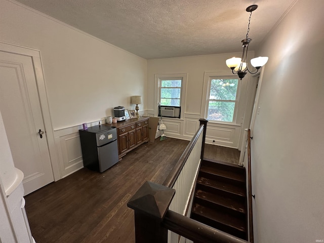 staircase featuring wainscoting, a decorative wall, wood finished floors, a textured ceiling, and a notable chandelier