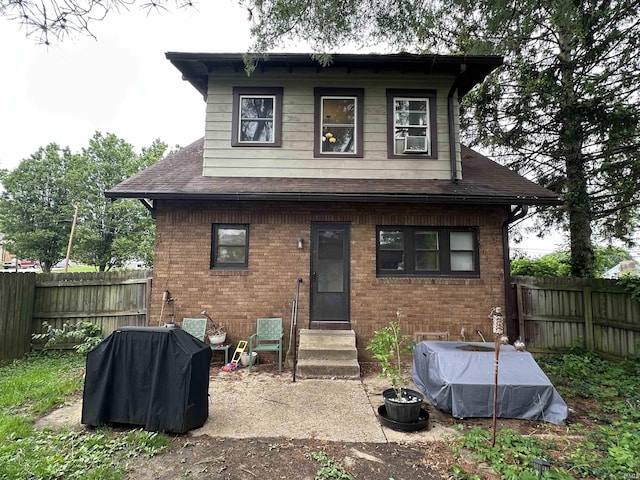rear view of house with brick siding, a shingled roof, a fenced backyard, and entry steps