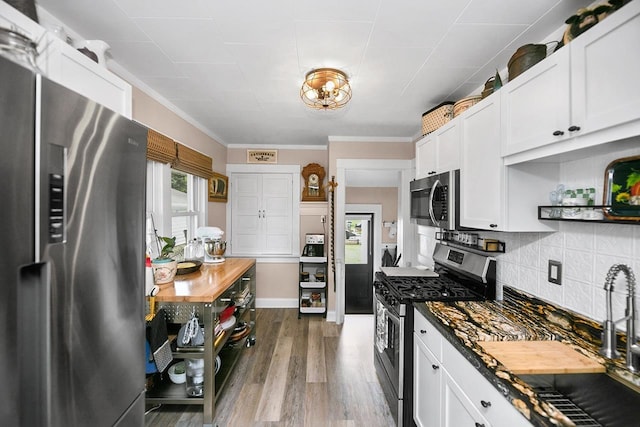 kitchen featuring dark countertops, appliances with stainless steel finishes, white cabinetry, decorative backsplash, and wood finished floors