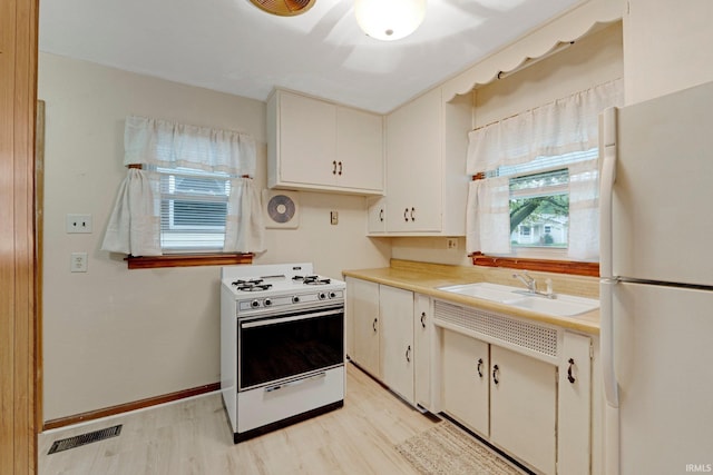 kitchen featuring visible vents, a sink, light wood finished floors, and white appliances