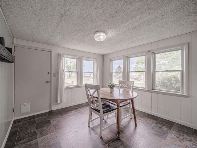 dining room with baseboards, wood walls, and a textured ceiling