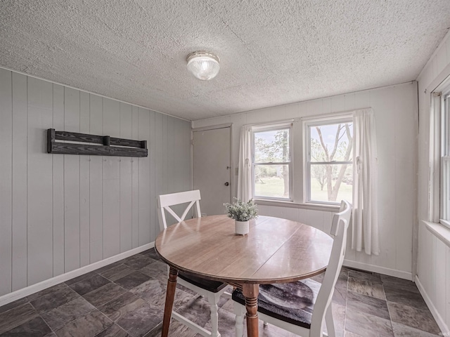 dining area with baseboards, wood walls, and a textured ceiling