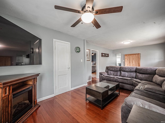 living area with baseboards, ceiling fan, a fireplace, and hardwood / wood-style flooring