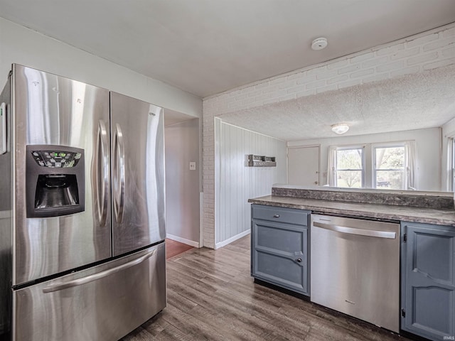 kitchen with blue cabinetry, appliances with stainless steel finishes, dark countertops, dark wood finished floors, and gray cabinetry