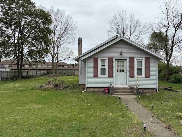 view of front facade featuring entry steps, fence, a chimney, and a front yard