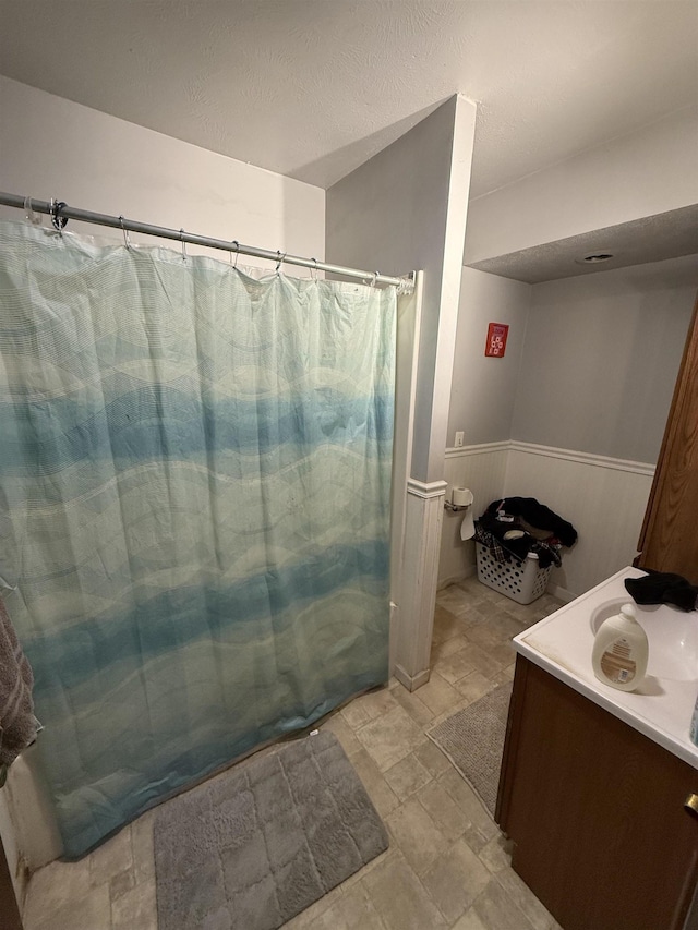 full bath featuring a shower with curtain, vanity, and wainscoting