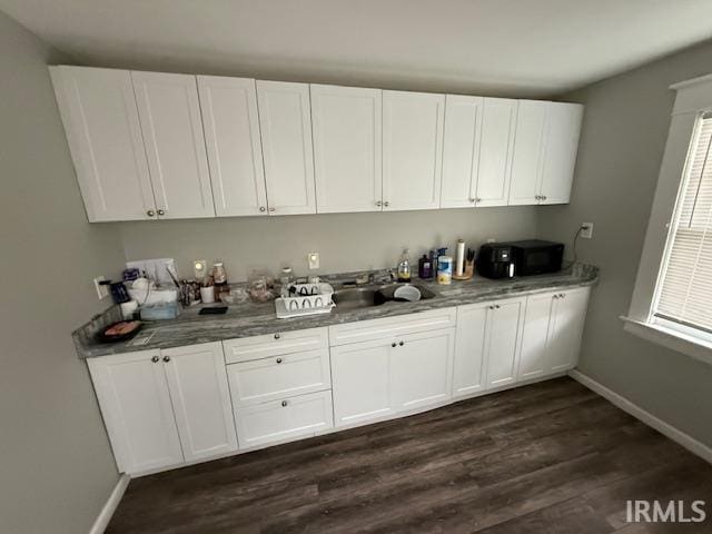 interior space with a sink, baseboards, and dark wood-type flooring