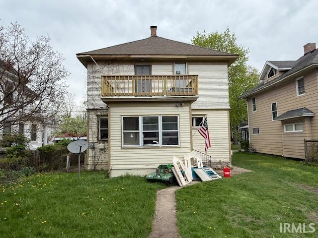 rear view of property featuring a lawn, a balcony, and a chimney