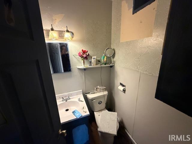 half bath featuring toilet, a textured wall, and vanity