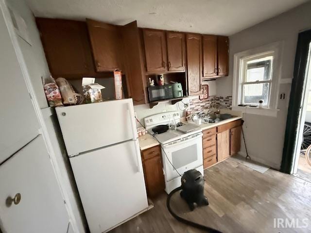 kitchen featuring brown cabinetry, light countertops, decorative backsplash, and white appliances