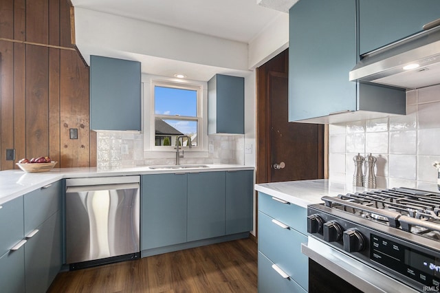 kitchen with wall chimney range hood, light countertops, tasteful backsplash, a sink, and appliances with stainless steel finishes