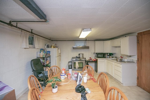 kitchen featuring light countertops, stainless steel gas stove, black microwave, and concrete block wall