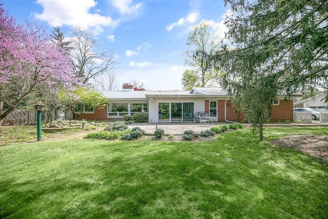 rear view of house featuring a yard, brick siding, a chimney, and a patio