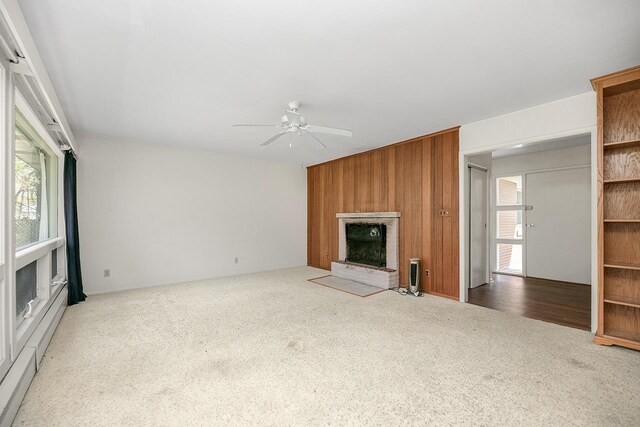unfurnished living room with carpet, ceiling fan, wooden walls, and a fireplace