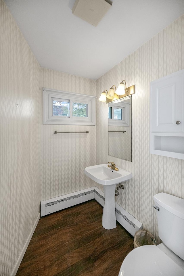 half bath featuring a baseboard heating unit, wood finished floors, toilet, and wallpapered walls