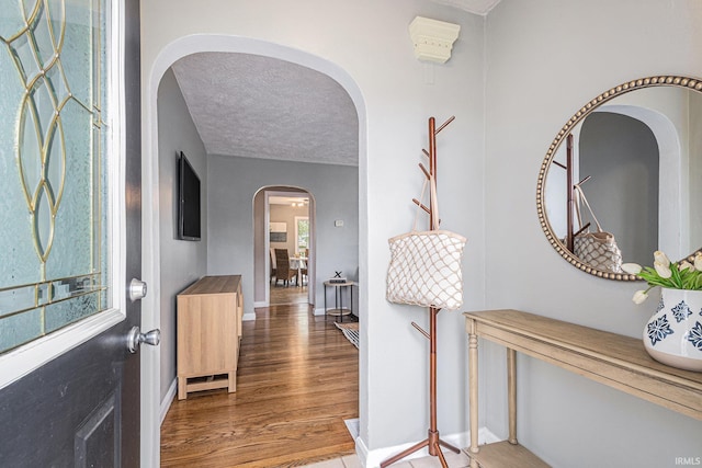 entryway with baseboards, arched walkways, a textured ceiling, and wood finished floors