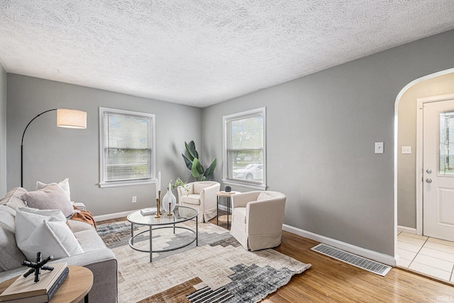 living room featuring arched walkways, visible vents, a wealth of natural light, and wood finished floors