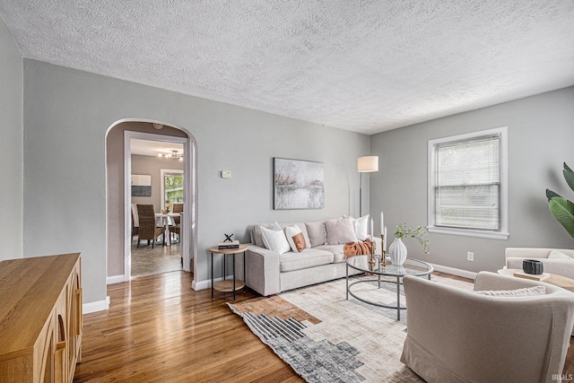 living area featuring arched walkways, baseboards, wood finished floors, and a textured ceiling