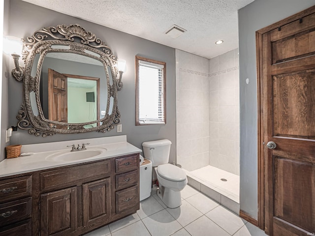 bathroom with tile patterned flooring, vanity, toilet, a textured ceiling, and tiled shower