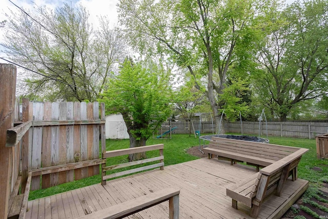 wooden terrace featuring a storage unit, a fenced backyard, a trampoline, and a yard