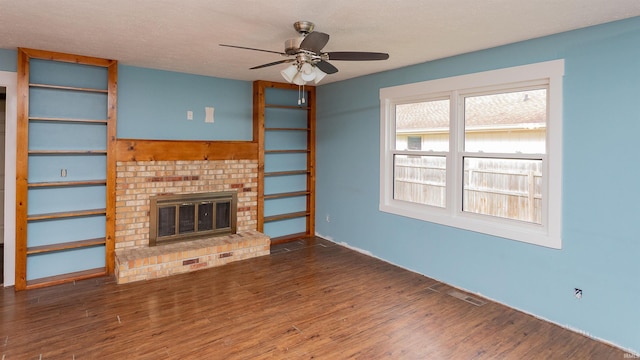 unfurnished living room featuring a brick fireplace, ceiling fan, visible vents, and wood finished floors