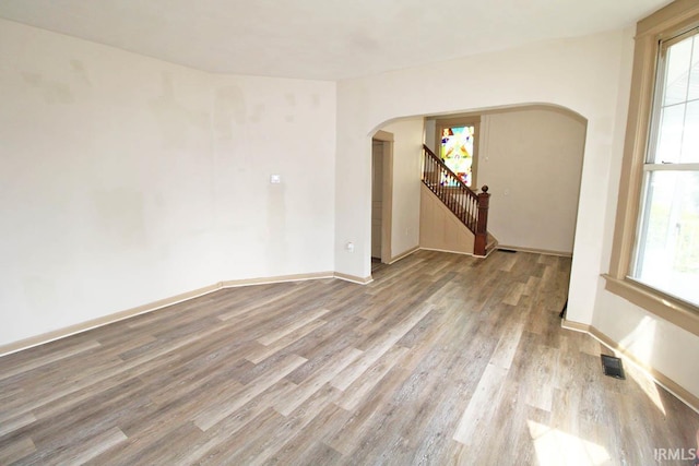 2813 W Franklin St, Evansville, IN 47712 - unfurnished room featuring visible vents, wood finished floors, baseboards, stairway, and arched walkways