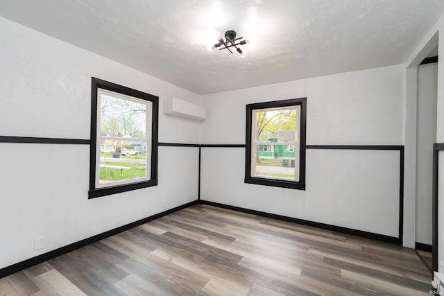 spare room with a wall mounted AC, wood finished floors, and a wealth of natural light