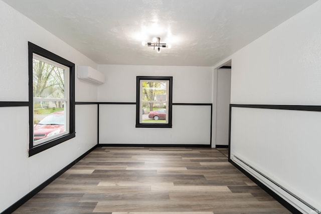 spare room with wood finished floors, a wall mounted AC, and baseboard heating