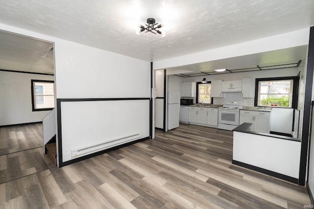 kitchen featuring white cabinetry, wood finished floors, baseboard heating, and white appliances