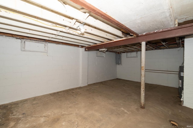 unfinished basement with concrete block wall, water heater, and electric panel