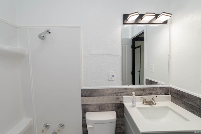 full bath featuring vanity, a bathing tub, toilet, and a wainscoted wall