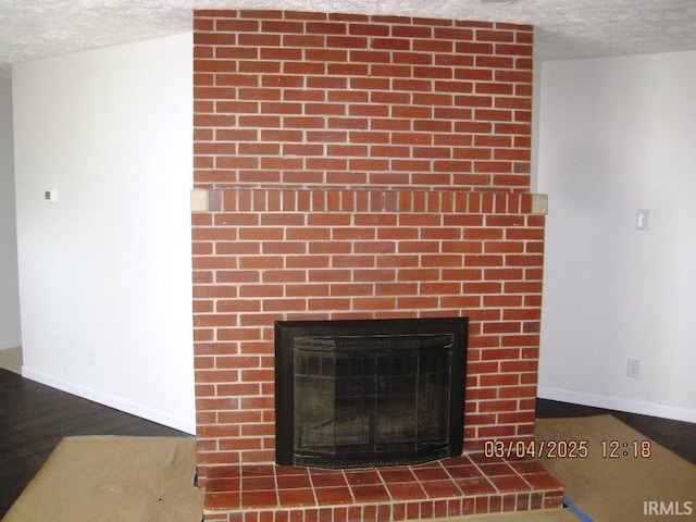 interior details with baseboards, a textured ceiling, wood finished floors, and a large fireplace
