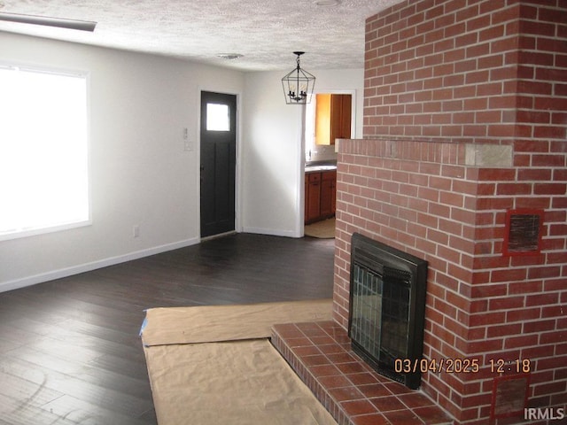 unfurnished living room featuring a fireplace with raised hearth, baseboards, dark wood-style floors, and a textured ceiling
