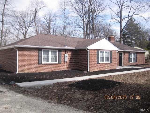 ranch-style home with brick siding, a chimney, and a shingled roof