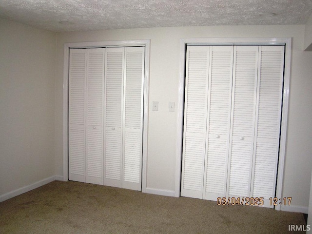 unfurnished bedroom featuring baseboards, two closets, carpet flooring, and a textured ceiling