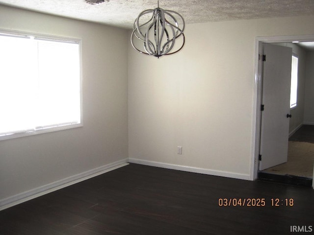 unfurnished dining area featuring baseboards, dark wood-type flooring, a textured ceiling, and a chandelier