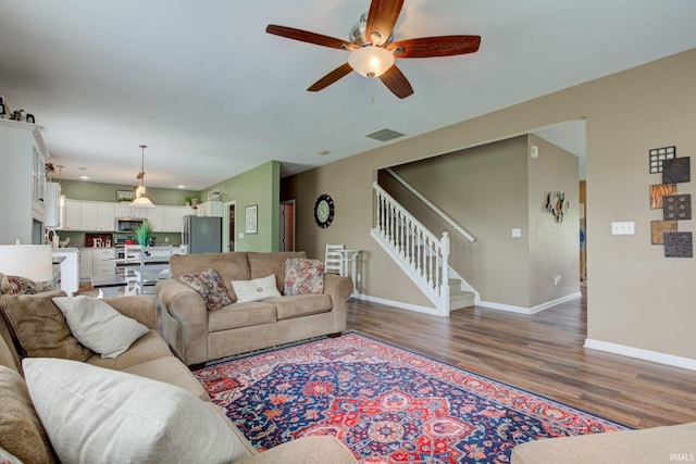 living area with visible vents, stairs, wood finished floors, baseboards, and a ceiling fan