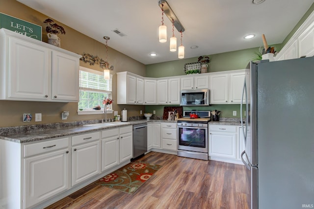 kitchen featuring white cabinets, a sink, stainless steel appliances, wood finished floors, and pendant lighting