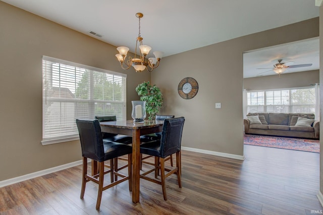 dining area featuring baseboards, ceiling fan with notable chandelier, wood finished floors, and visible vents